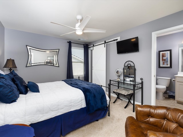 bedroom featuring a barn door, ensuite bath, light colored carpet, and ceiling fan
