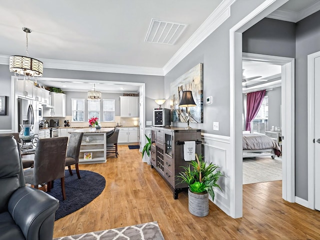 living room with visible vents, light wood-style floors, ornamental molding, and a healthy amount of sunlight