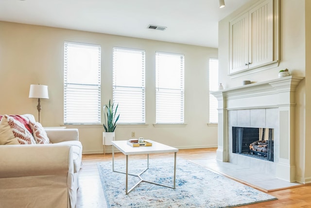 living area featuring baseboards, a tile fireplace, visible vents, and light wood-style flooring