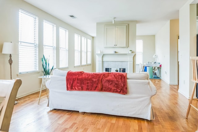 living room featuring plenty of natural light, a tiled fireplace, and light wood-style flooring