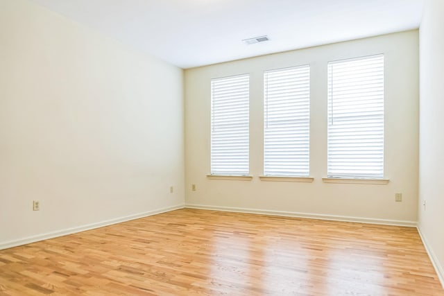 unfurnished room with light wood-type flooring, visible vents, and baseboards