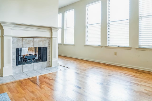unfurnished living room featuring baseboards, wood finished floors, and a tiled fireplace