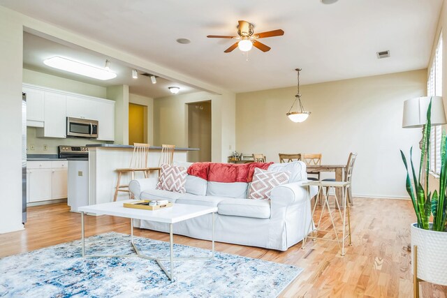living room featuring light wood finished floors, visible vents, a ceiling fan, and baseboards