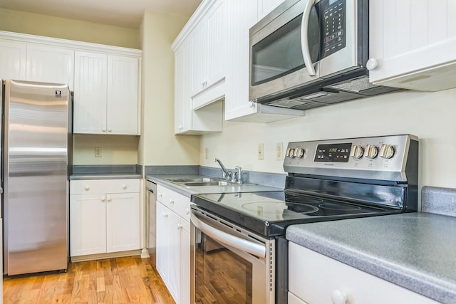 kitchen featuring light wood-type flooring, appliances with stainless steel finishes, white cabinetry, and a sink