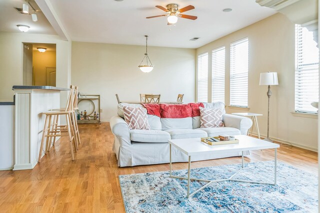 living area featuring light wood finished floors, a ceiling fan, baseboards, and a wealth of natural light