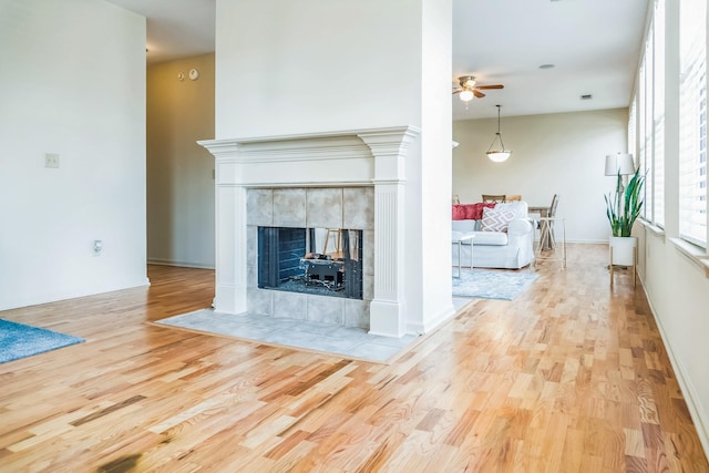 living area featuring wood finished floors, a tiled fireplace, a ceiling fan, and baseboards