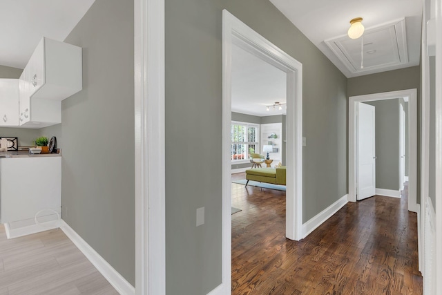 hall featuring attic access, baseboards, and wood finished floors