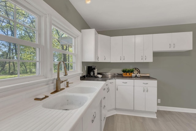 kitchen with a healthy amount of sunlight, baseboards, white cabinetry, and a sink