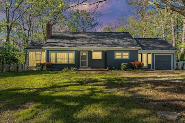 view of front facade with an attached garage, a chimney, fence, and a lawn