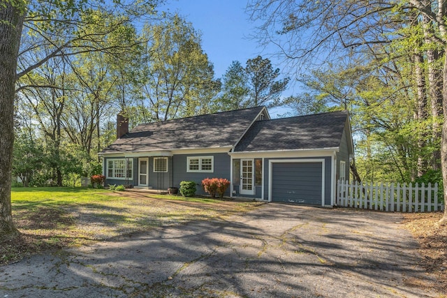 view of front of house with a chimney, a front lawn, aphalt driveway, an attached garage, and fence