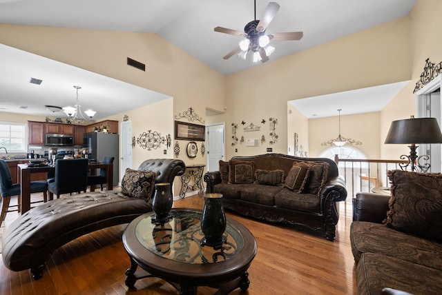 living area featuring light wood-style flooring, visible vents, high vaulted ceiling, and ceiling fan with notable chandelier
