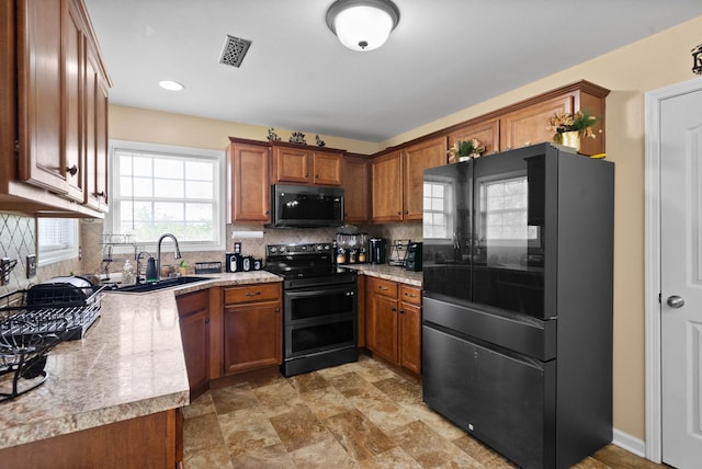 kitchen featuring brown cabinetry, decorative backsplash, a sink, and black appliances