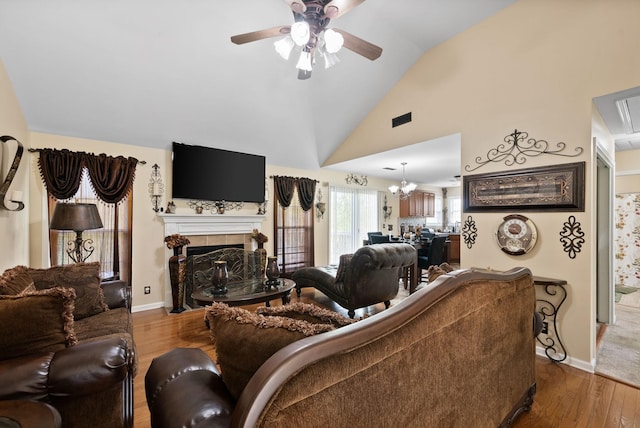 living area featuring a ceiling fan, wood finished floors, a tiled fireplace, baseboards, and lofted ceiling