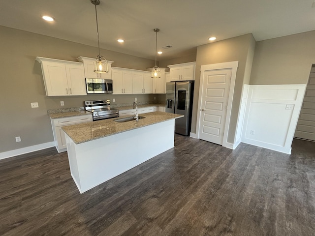kitchen with stainless steel appliances, a sink, a center island with sink, white cabinetry, and light stone counters