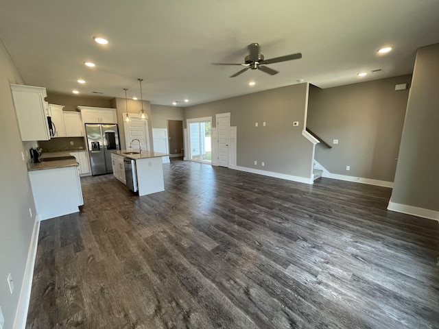 kitchen with open floor plan, a kitchen island with sink, ceiling fan, stainless steel appliances, and baseboards