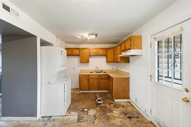 kitchen featuring brown cabinets, under cabinet range hood, visible vents, a sink, and stacked washing maching and dryer