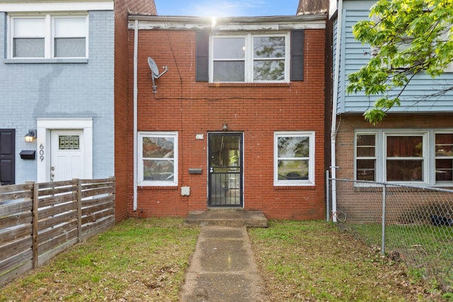 multi unit property with brick siding, a front lawn, and fence