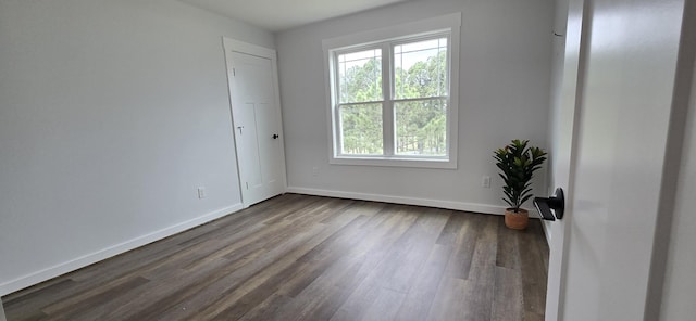 spare room with baseboards and dark wood-type flooring