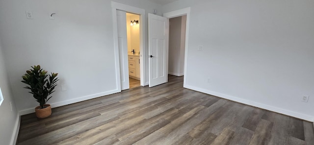 unfurnished bedroom with ensuite bath, baseboards, and wood finished floors