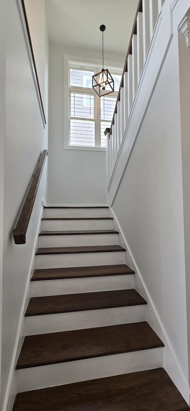 stairs with wood finished floors and an inviting chandelier