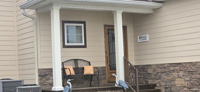 view of exterior entry featuring stone siding, a porch, and central air condition unit