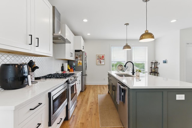 2006 Manchester Ave, Nashville, TN 37218 - kitchen featuring white cabinets, light wood finished floors, stainless steel appliances, wall chimney range hood, and a sink