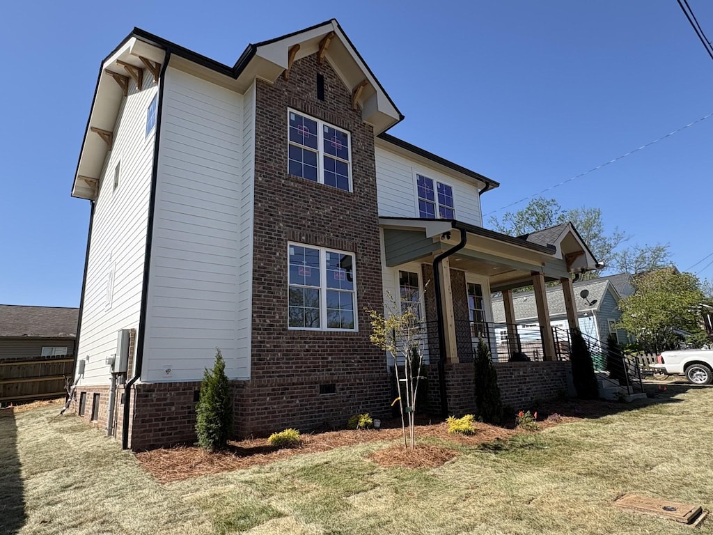 view of side of home featuring a lawn, brick siding, a porch, and crawl space
