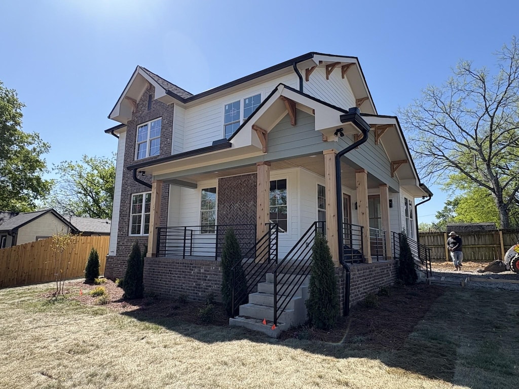 view of front facade with brick siding, covered porch, and fence
