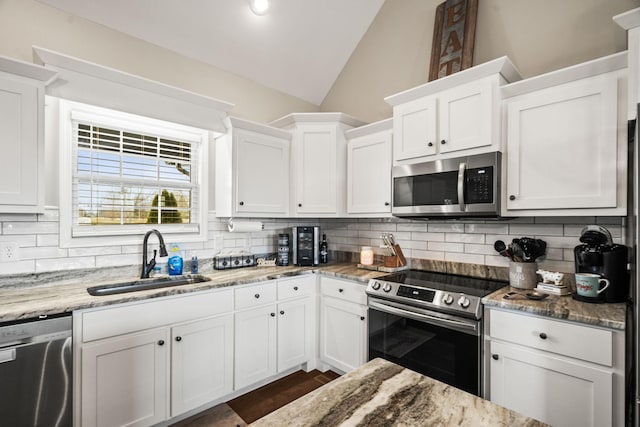 kitchen featuring vaulted ceiling, a sink, decorative backsplash, stainless steel appliances, and white cabinets