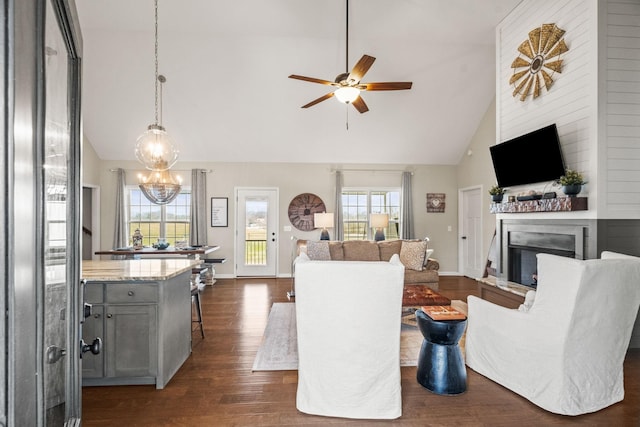 living area with high vaulted ceiling, ceiling fan with notable chandelier, a fireplace, baseboards, and dark wood-style floors
