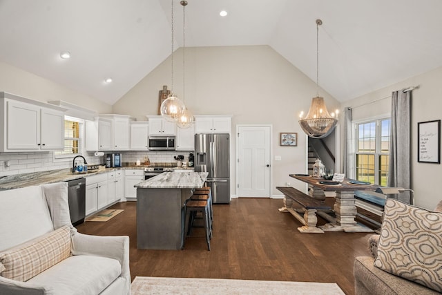 kitchen with a sink, an inviting chandelier, a kitchen bar, high vaulted ceiling, and appliances with stainless steel finishes