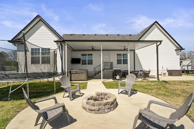 back of property with a patio area, a trampoline, a ceiling fan, an outdoor fire pit, and a hot tub