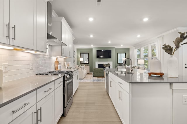 kitchen with wall chimney range hood, a sink, stainless steel gas range, open floor plan, and ornamental molding