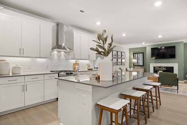 kitchen with a breakfast bar, a kitchen island with sink, light wood-type flooring, backsplash, and wall chimney exhaust hood