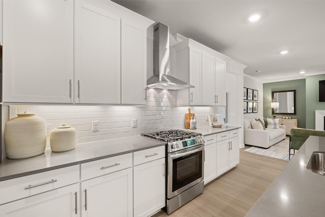 kitchen with tasteful backsplash, open floor plan, stainless steel gas stove, wall chimney exhaust hood, and white cabinetry