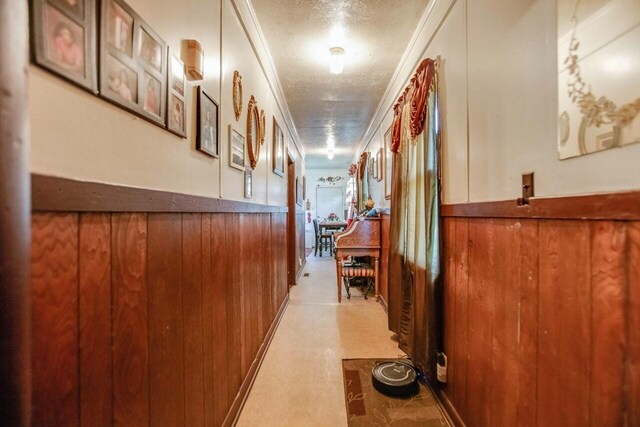 hall featuring crown molding, a textured ceiling, a wainscoted wall, and wood walls