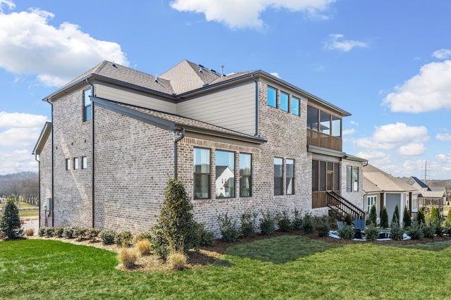 rear view of property featuring brick siding, a yard, and a shingled roof