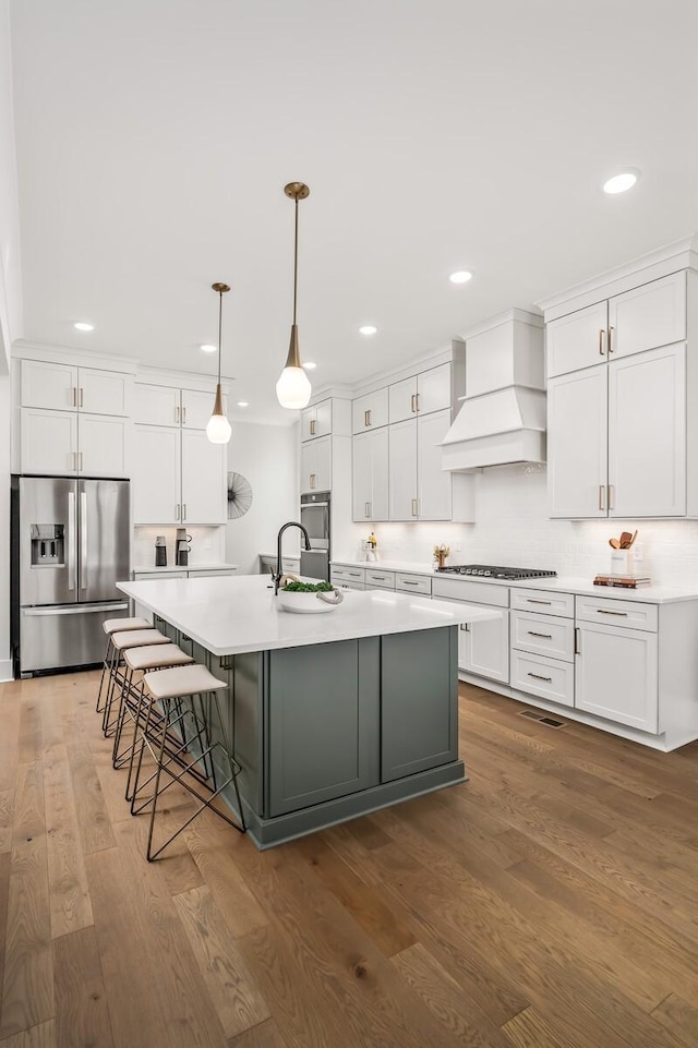 kitchen featuring stainless steel appliances, a spacious island, custom exhaust hood, white cabinetry, and wood finished floors