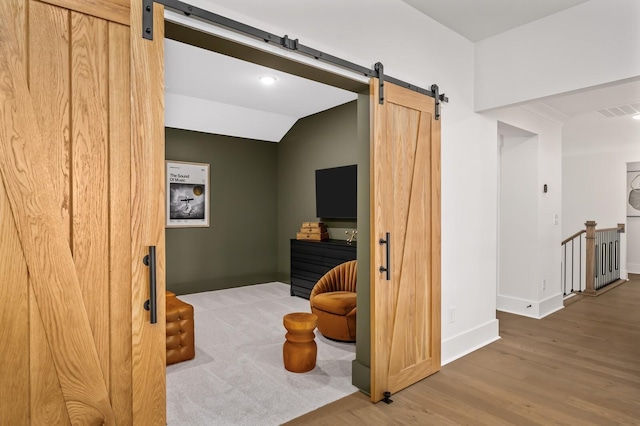 interior space with a barn door, an upstairs landing, wood finished floors, baseboards, and visible vents