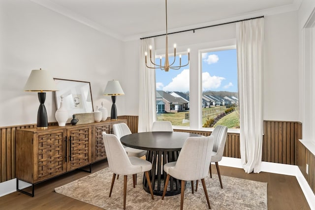 dining space with a wainscoted wall, wood finished floors, an inviting chandelier, and ornamental molding