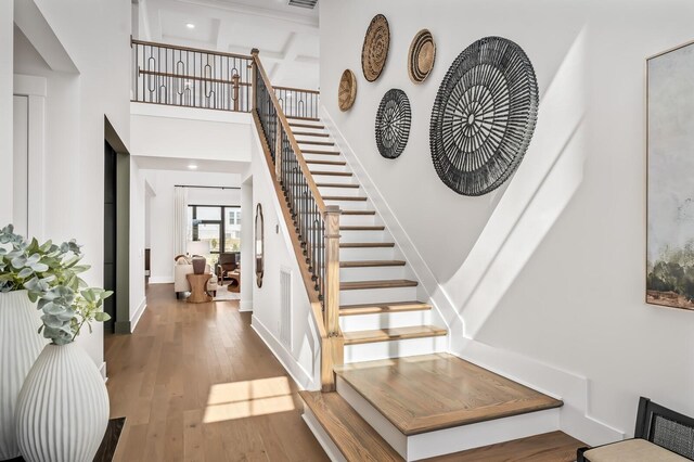 stairs featuring visible vents, baseboards, wood finished floors, and a towering ceiling