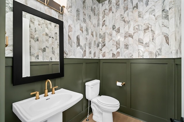 bathroom featuring wood finished floors, toilet, a sink, a decorative wall, and wainscoting