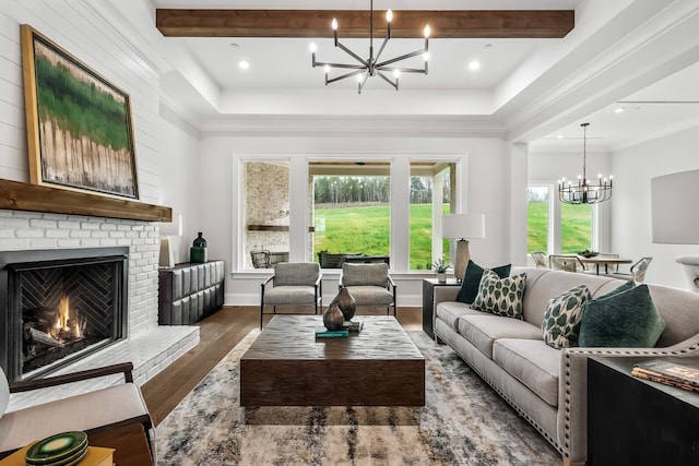 living room with wood finished floors, an inviting chandelier, beamed ceiling, ornamental molding, and a brick fireplace