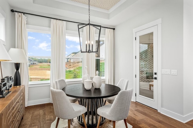 dining space featuring baseboards, a tray ceiling, a notable chandelier, and dark wood-style flooring