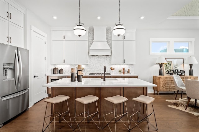 kitchen with decorative backsplash, premium range hood, a breakfast bar area, and stainless steel fridge with ice dispenser