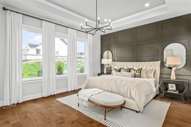 bedroom featuring a decorative wall, a notable chandelier, a tray ceiling, and recessed lighting
