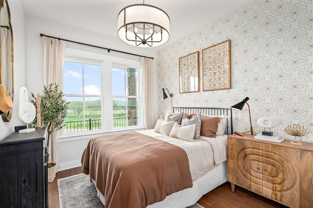 bedroom featuring baseboards, wood finished floors, multiple windows, and wallpapered walls