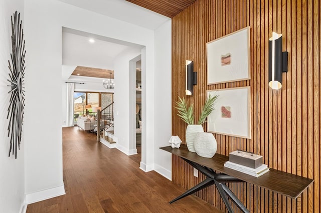 hallway with an inviting chandelier, wood walls, wood finished floors, and baseboards