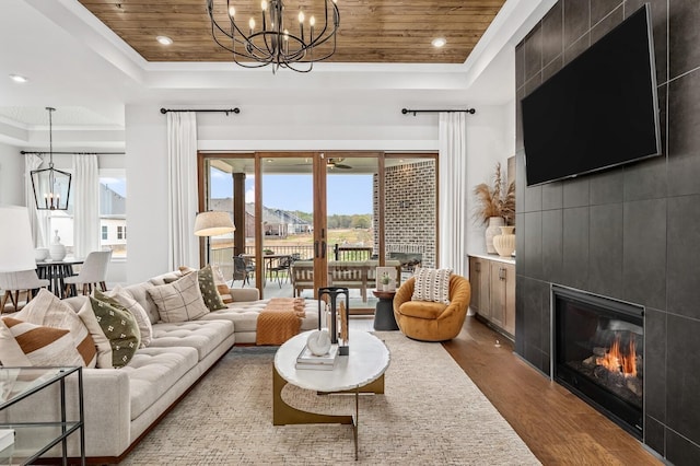 living area with a tray ceiling, wood finished floors, a fireplace, wood ceiling, and a chandelier