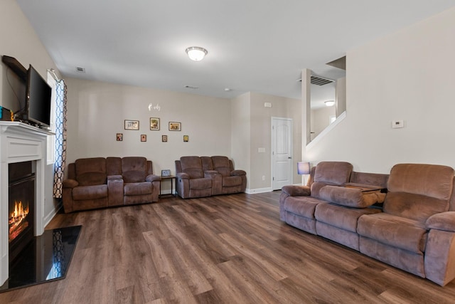 living area featuring visible vents, baseboards, wood finished floors, a warm lit fireplace, and stairway